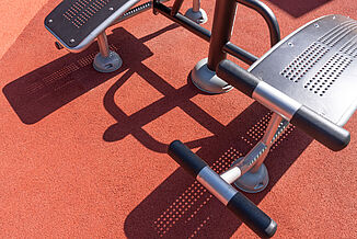 Detailaufnahme des fugenlos verlegten REGUPOL Fallschutz- und Spielfeldbodens unter Outdoor-Fitnessgeräten auf einer barrierefreien Spiel- und Bewegungsfläche in Berlin-Steglitz-Zehlendorf.