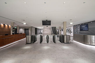 Entrance area with tiled floor, reception and staircase with escalator in the Silvretta Therme in Ischgl.