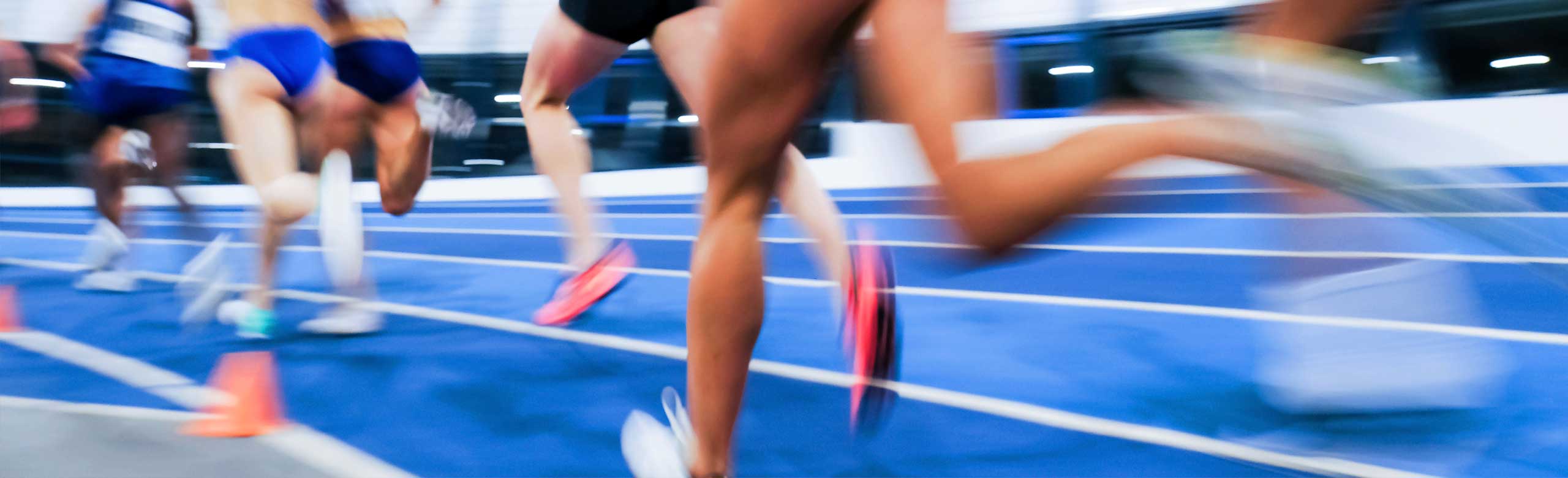 Dynamisches Bild eines Leichtathletik-Rennens, Läuferinnen sprinten auf blauer Laufbahn, Bewegungsunschärfe betont Geschwindigkeit und Intensität des Wettkampfs.