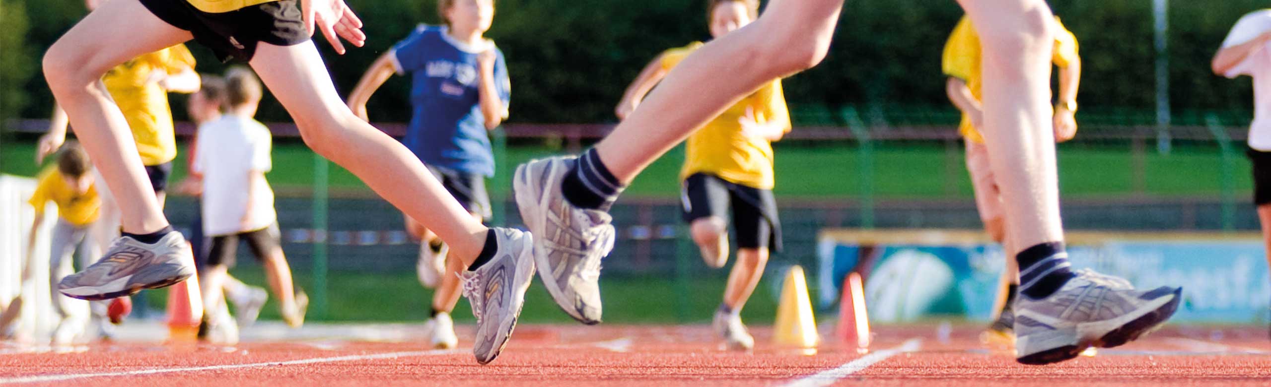 Kinder auf REGUPOL Laufbahn beim Training oder Spiel. Kinder und Jugendliche laufen und spielen auf einer roten Kunststoff-Laufbahn bei sonnigem Wetter im Stadion.