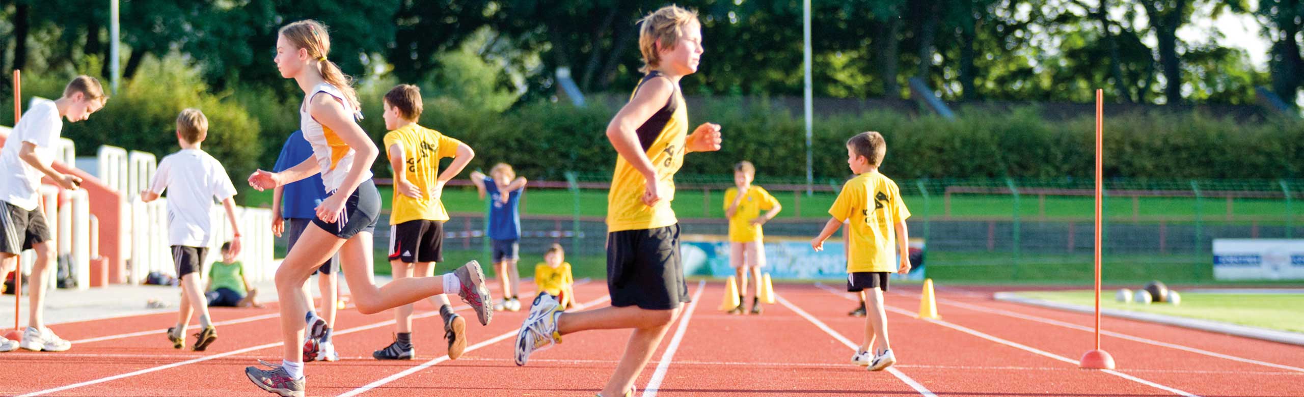 Children on REGUPOL track during training or play. Children and young athletes running and playing on a red synthetic track under sunny skies at the stadium.