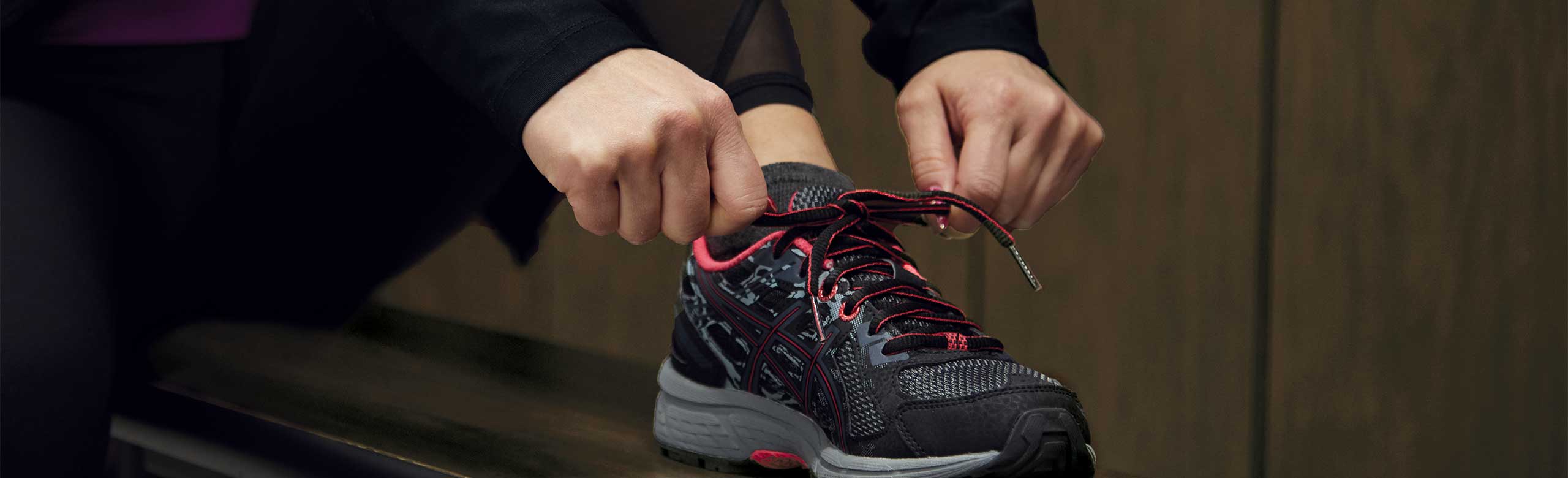 Eine Person bindet sich auf einer Bank in einer Umkleidekabine einen Schuh. Eine Person bindet sich auf einer Bank in einer Umkleidekabine einen Schuh.