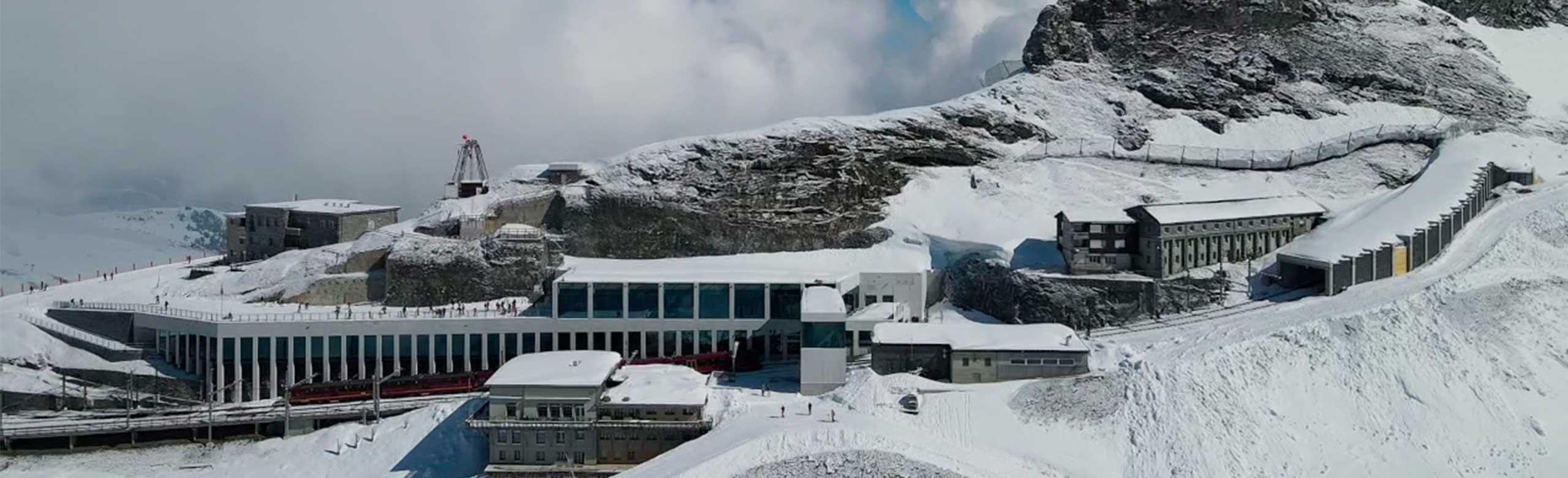 Außenansicht einer Bergstation einer Bergbahn. Die Bergstation befindet sich auf einem Berg. Der Berg und auch die Bergstation sind mit Schnee bedeckt. 