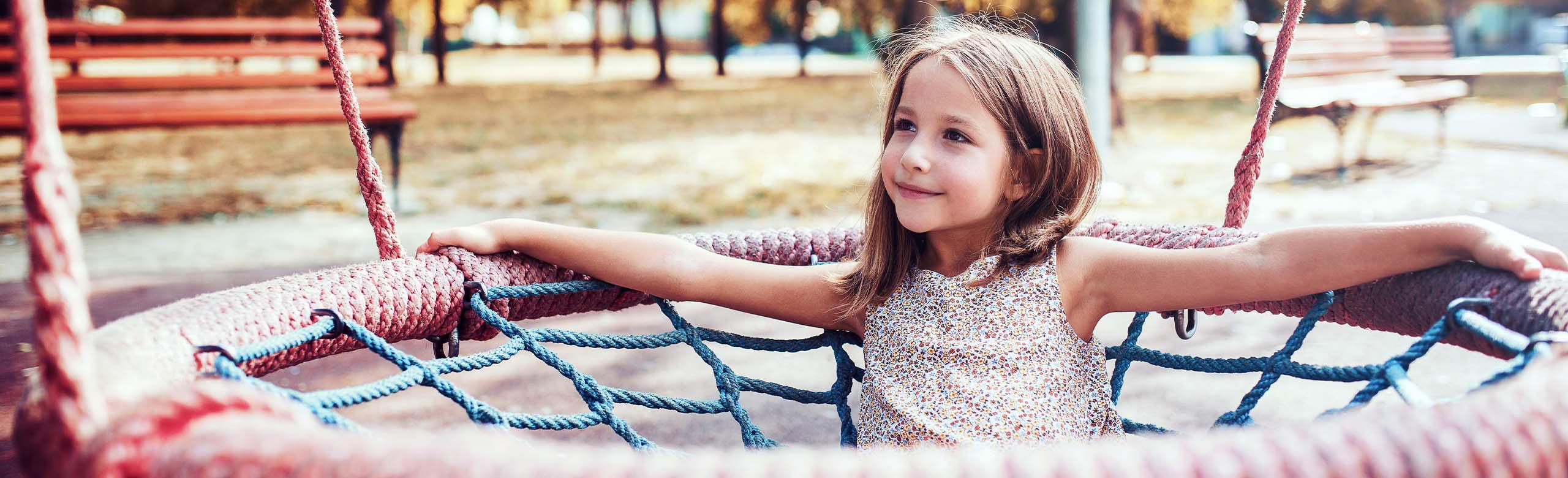 Smiling child in a nest swing on a playground with REGUPOL playfix block step - elastic block step for edging play and sports areas