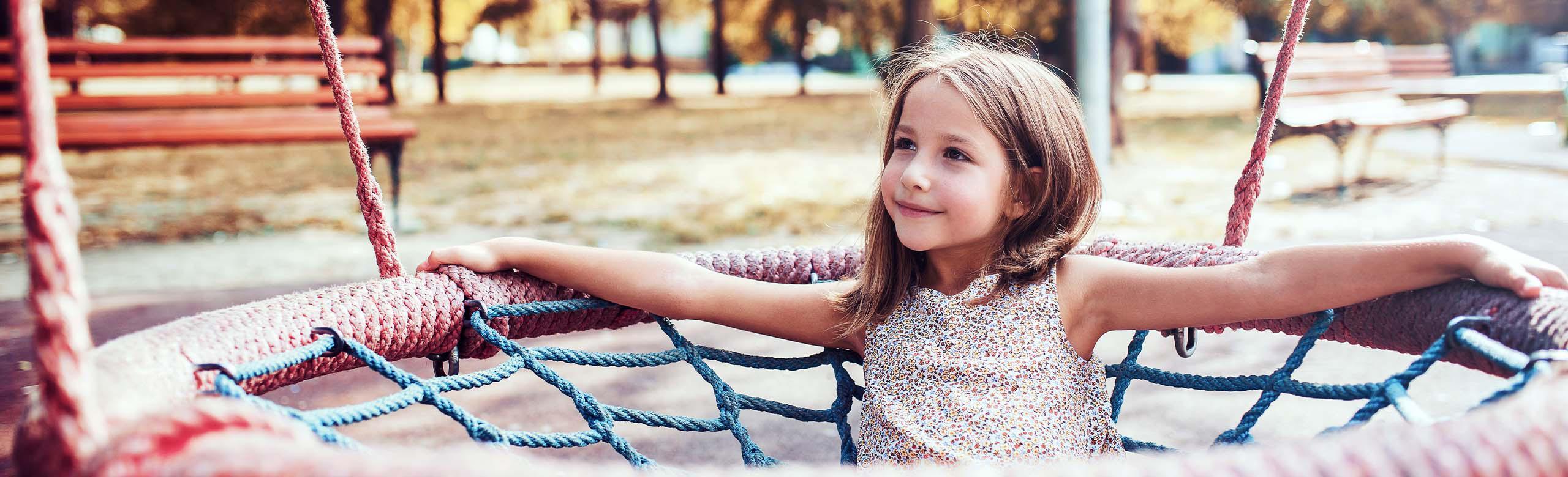 Smiling child in a nest swing on a playground with built-in REGUPOL playfix bollard - shock-absorbing and elastic boundary bollard for more safety in the play area