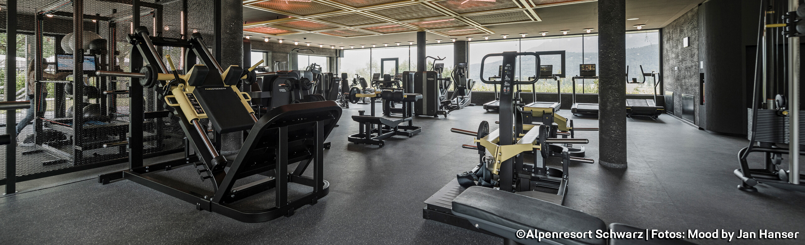 Trainingsgeräte im Fitnessstudio Ein Fitnessstudio in einem Hotel mit vielen Trainingsgeräten und einem dunkel gehaltenen Boden. Am Ende des Raumes ist eine große Fensterfront.